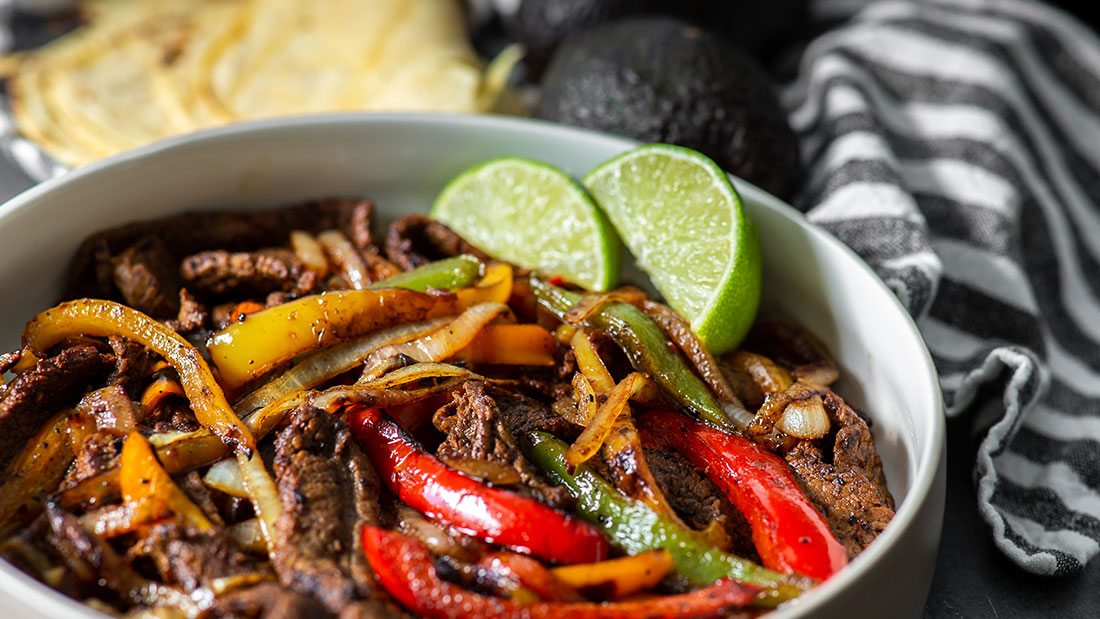 close up of chili lime steak fajitas with tortillas and avocados and lime